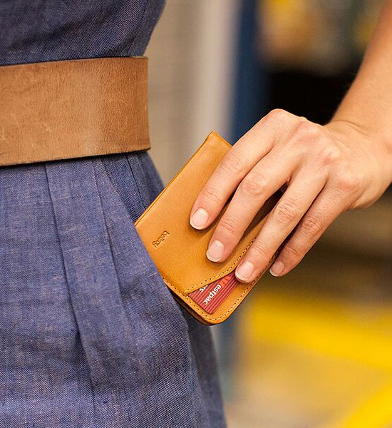 女性が前ポケットにキャリーアウトウォレットキャラメル付属の極薄二つ折り財布を収納する写真