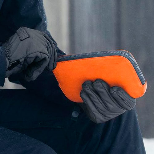スノーウェアで手袋をしたままオールコンディションズエッセンシャルズポケットバーントオレンジのファスナーを開こうとしている男性のイメージ