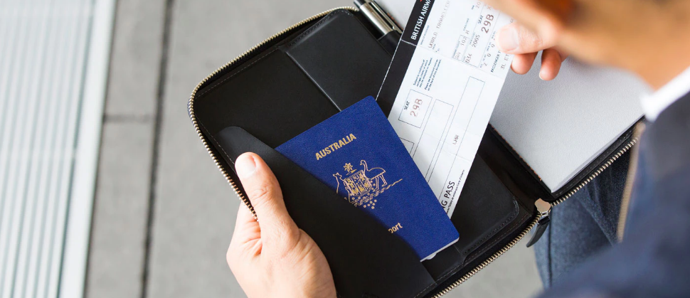 パスポート、ペン、ノートの収納されたBellroy Work Folio Blackから航空チケットを取り出す男性の写真